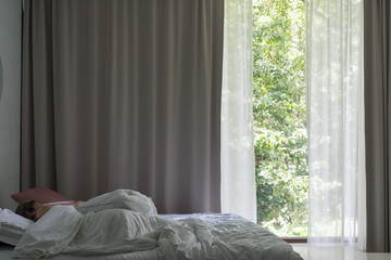 Asian woman sleeping in bed with curtains and forest background