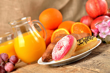 Sweet breakfast, donuts, oranges and orange juice and spring flowers on wooden table