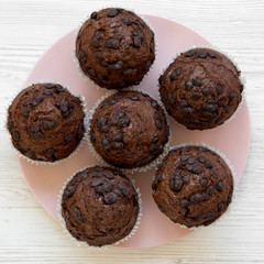 Tasty chocolate muffins on pink plate on white wooden background, overhead view. Flat lay, top view, from above. Close-up.