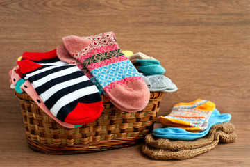 Basket with different socks. Socks of different sizes in a large wicker basket. Clothing for autumn and winter in the form of socks. A pile of colorful socks on a wooden background.