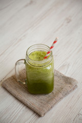 Glass jar of green celery smoothie on white wooden table, low angle view.