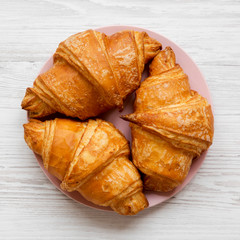 Fresh croissants with golden crust on white wooden table, overhead view. From above, flat lay.