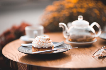 Tasty creamy cake on plate with glass teapot and cup on wooden table. Good morning. Breakfast.