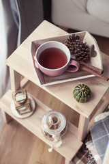 Plaids, a cup of hot tea, autumn decor, a book, a pumpkin on a wooden chair. Cozy, autumn decor. Autumn interior, sofa. Autumn. Winter.