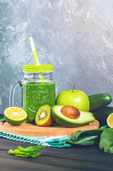 healthy green smoothie with ingredients on a wooden table: apple, kiwi, lime, spinach, mint, avocado, cucumber