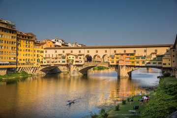 Yoga on the banks of the river Arno, while a kayak paddles under the Ponte Vecchio in Florence