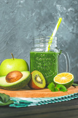 healthy green smoothie with ingredients on a wooden table: apple, kiwi, lime, spinach, mint, avocado, cucumber