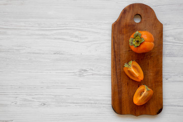 Fresh persimmon on a chopping board on white wooden background, top view. Flat lay, overhead, from above. Copy space and text area.