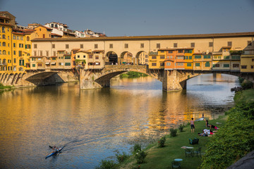 Yoga on the banks of the river Arno, while a kayak paddles under the Ponte Vecchio in Florence