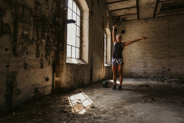 Obraz na płótnie Canvas Athletic woman holding kettlebell up in an old building