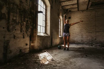 Fotobehang Athletic woman holding kettlebell up in an old building © sasamihajlovic