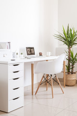Modern hipster workplace. Small white office with table, chair, notebook, cup and plant
