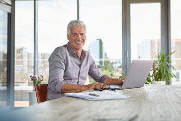 Fototapeta na wymiar Portrait of smiling mature man using laptop on table at home