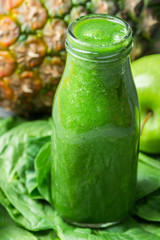 Bottle with Green Fresh Raw Smoothie from Leafy Greens Vegetables Fruits Apples Pineapple Bananas Kiwi Zucchini on Scattered Spinach Leaves. Healthy Lifestyle Detox Vitamins Energy Concept