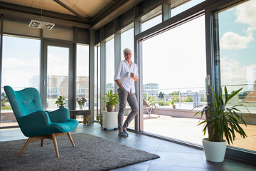Portrait of smiling mature man holding coffee cup standing at the window at home
