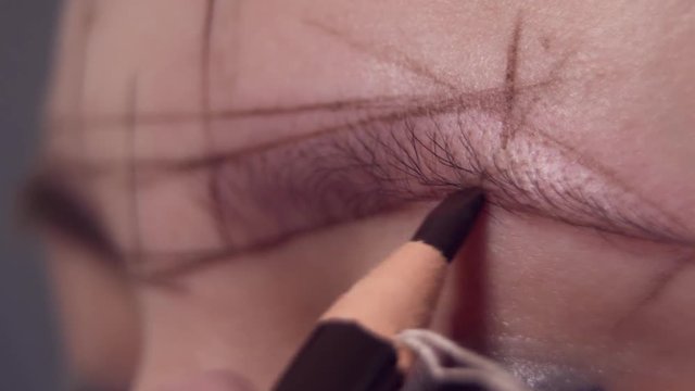 drawing contours on the eyebrows of a woman for applying permanent makeup in a beauty salon