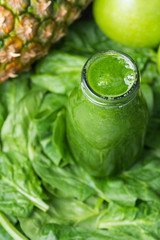 Bottle with Green Fresh Raw Smoothie from Leafy Greens Vegetables Fruits Apples Pineapple Bananas Kiwi Zucchini on Scattered Spinach Leaves. Healthy Lifestyle Detox Vitamins Energy Concept. Copy space
