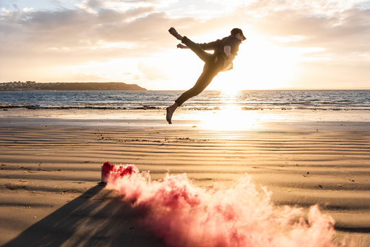 Man doing movement training at the beach with colorful smoke at sunset