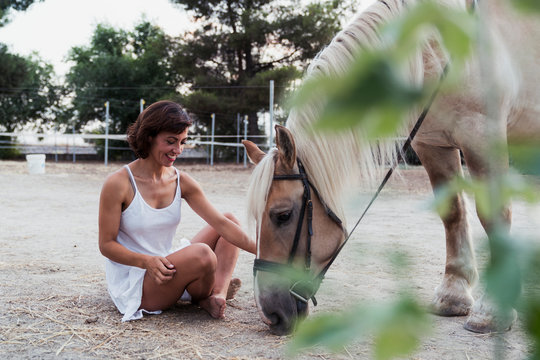 Smiling woman sitting on the ground watching horse