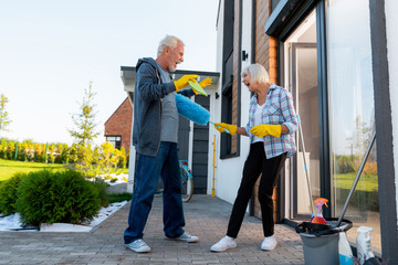 Cleaning territory. Modern laughing grandmother and grandfather having fun while cleaning territory near summer house