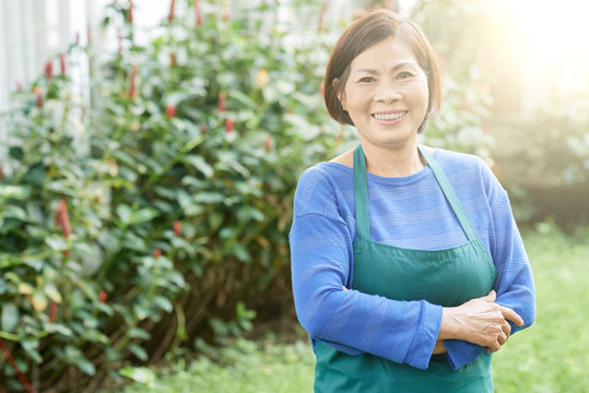 Portrait of mature smiling woman in apron standing in her garden outdoors