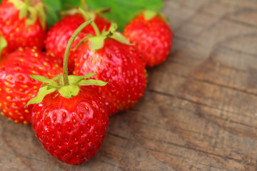 Bright ripe strawberries lying on a wooden table with green leaves. Close up view from top. 