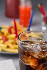 fizzy drink with ice in a glass on the background of a plate with fried potatoes