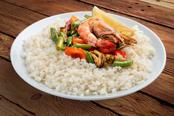 Rice porridge with shrimps and vegetables. On a wooden background