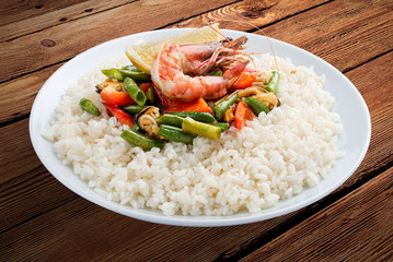 Rice porridge with shrimps and vegetables. On a wooden background