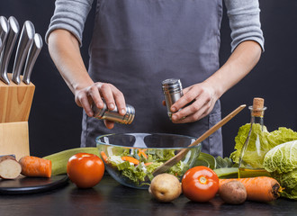 The hands of a woman cook prepare a salad with fresh vegetables. Healthy food. Black background