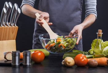 The hands of a woman cook prepare a salad with fresh vegetables. Healthy food. Black background