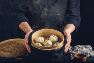 Woman presenting dim sum dumplings in steamer - obrazy, fototapety, plakaty