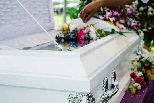 A hand offering a flower to the dead on the coffin during mourning and funeral rites at the cemetery ground.