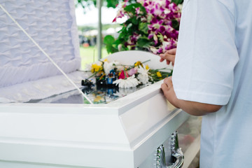 Unrecognizable person in white shirt mourns at the coffin of the dead family member.