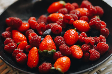 fresh raspberries and strawberries on a black plate.