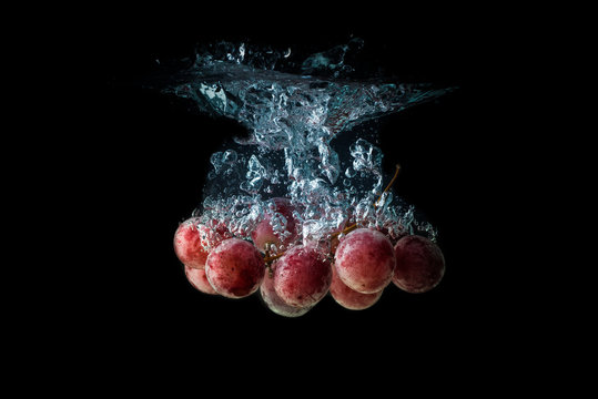 Red grapes splashing and sinking in water on black background with air bubbles.