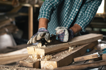 Close-up of the hands of a gloved carpenter with a hand planer handles wood
