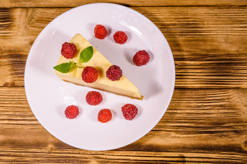 White plate with cheesecake New York, leaf of mint and raspberries on wooden table. Top view