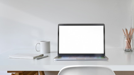 Blank white screen laptop with office supplies on white desk workspace.