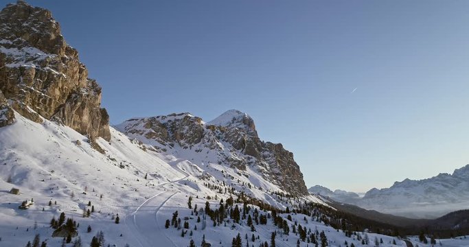 Forward aerial to snowy valley with woods forest and ski track at falzarego pass.Sunset or sunrise, clear sky.Winter Dolomites Italian Alps mountains outdoor nature establisher.4k drone flight