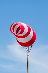 Windsock on blue sky background. Red and white stripe textile in wind with slightly cloudy sky....