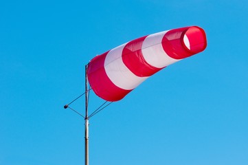 Windsock on blue sky background. Red and white stripe textile in wind with slightly cloudy sky. Indicating direction and speed of wind.