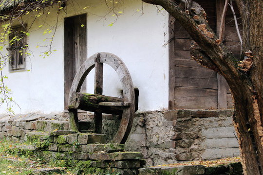 An old house and an old windmill wheel that pumps water.
