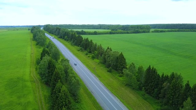 Road with moving cars between green agricultural fields, aerial shot