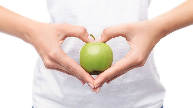 Woman making hands in heart shape and holding apple