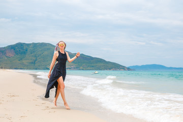 Obraz na płótnie Canvas beautiful girl in a black dress walks on the beach