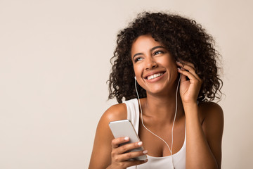 Smiling african-american woman in earbuds listening music - obrazy, fototapety, plakaty