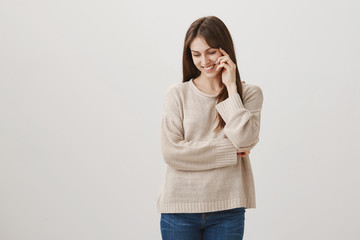 You make me blush. Studio shot of shy friendly caucasian woman in casual clothes looking down with cheerful smile and holding fingers on face, walking with her dog in park, being moved with cuteness © Cookie Studio