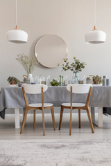 White chairs at table in elegant dining room interior with round mirror and lamps. Real photo