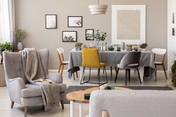 Blanket on grey armchair in spacious dining room interior with chairs at table. Real photo